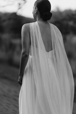 Dalgalı beyaz elbiseli bir mankenin huzurlu bir arka görüntüsü, sakin bir açık hava ortamında güzel bir şekilde yakalandı.
