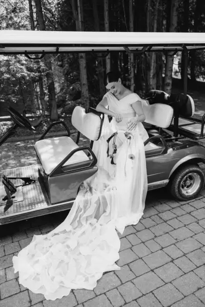 Güzel bir gelin, zarif ve zarif bir şekilde, çarpıcı bir gelinlikle bir golf arabasının yanında poz verir.