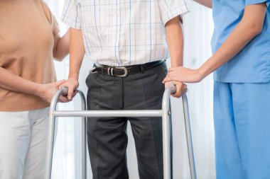 Contented senior man walking as he is helped by his wife and caretaker, walking with the aid of a folding walker. Nursing home for the elderly concept.