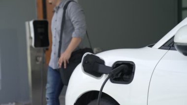 Adamın biri evinde elektrikli araç şarj aletinin fişini çekiyor. İlerici bir yaşam tarzında elektrikli araçların kullanımı, temiz ve sağlıklı bir çevreye katkıda bulunur..