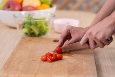 Close up hands holding a knife preparing a contented meal. Sliced tomatoes and other vegetables on the glass dish.