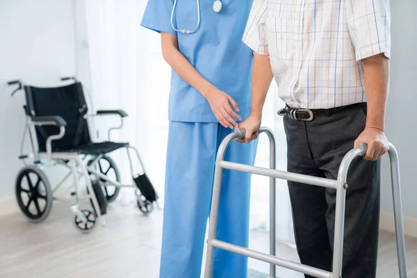 stock image Physiotherapist assists contented senior man on folding walker. Recuperation for elderly, seniors care, nursing home.