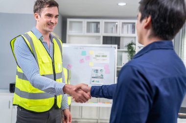 An engineer with a protective vest handshake with an investor in his office. Following a successful meeting, employee and employer form a partnership.