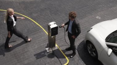 İlerici işadamı, şehir merkezinde dolaşmadan önce şarj cihazından elektrikli arabasına şarj prizi takıyor. Çevre dostu şarj edilebilir araba, sürdürülebilir ve temiz enerjiyle çalışıyor..