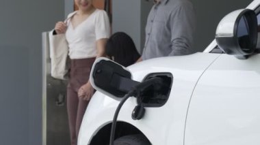 İlerici ebeveynler kızlarını okuldan alırken elektrikli araba ve yenilenebilir enerji kavramını kullandılar, evdeki EV otomobil için şarj istasyonu. Alternatif eko taşımacılığı.
