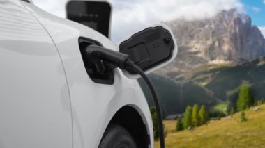 Temiz çevre için temiz enerjinin yol açtığı ilerici elektrikli araba kavramının arka planı olarak dağın tepesinde bulutun zaman kavramının yer aldığı doğal manzara. EV araba şarj istasyonunda şarj oluyor..