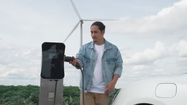 电动汽车是一个进步的人 他的电动汽车 电动汽车用风力涡轮机作为未来可持续能源的概念 从绿地的充电站向能源充电 配备发电机的电动车 — 图库视频影像