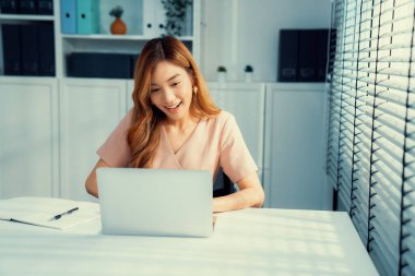 A young Asian female employee sitting at her desk in her office, sitting at desktop in workstation.