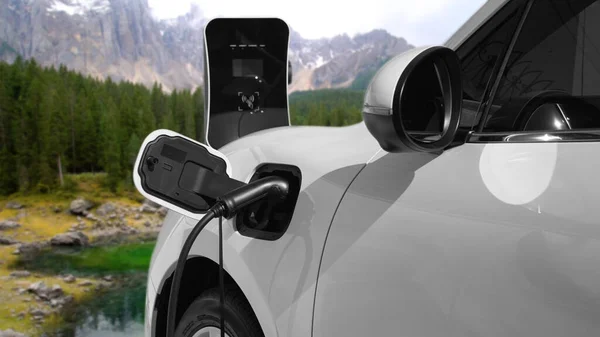 電気発生器ドライブによるエネルギー持続可能な車の電源 プログレッシブ旅行の概念のための山の背景と充電ステーションでバッテリーを充電します クリーン環境のシンボルとして自然界のEv車 — ストック写真