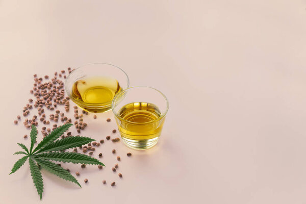 Масло CBD, тонус THC в стеклянной чаше и бутылка с крышкой капельницы и листья конопли на пустом фоне с грудой сухих семян конопли окружены минимализмом. Концепция легализации марихуаны.
