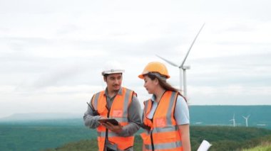 Erkek ve kadın mühendisler kırsal kesimdeki bir tepenin tepesinde ya da dağda rüzgar çiftliğinde çalışıyorlar. Yenilenebilir ve sürdürülebilir enerjinin gelecekteki üretimi için yenilikçi idealler.