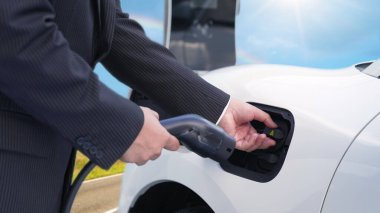 İlerici adam, yeşil çevre için yenilenebilir ve temiz enerjiyle çalışan EV otomobili hedefine ulaşmadan önce uzak bölgedeki şarj istasyonundan enerjiyi şarj etmek için duruyor.