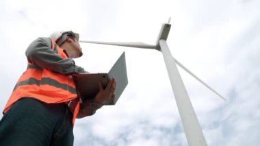 Gökyüzü arka planına sahip bir rüzgar türbini üzerinde çalışan mühendis. Yenilenebilir ve sürdürülebilir enerjinin gelecekteki üretimi için yenilikçi bir ideal. Rüzgar türbininden enerji üretimi.