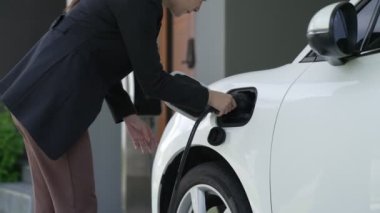 Bir kadın evinde elektrikli araç şarj aletinin fişini çekiyor. İlerici bir yaşam tarzında elektrikli araçların kullanımı, temiz ve sağlıklı bir çevreye katkıda bulunur..