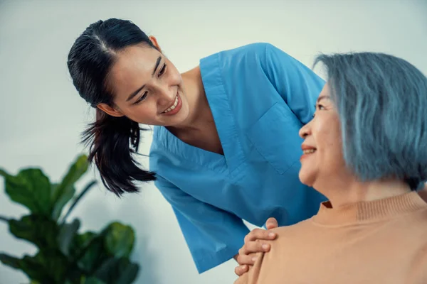 stock image A caregiver rest her hands on the shoulders of a contented senior patient while she sitting on the sofa at home.