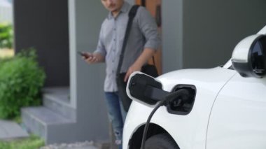 Adamın biri evinde elektrikli araç şarj aletinin fişini çekiyor. İlerici bir yaşam tarzında elektrikli araçların kullanımı, temiz ve sağlıklı bir çevreye katkıda bulunur..