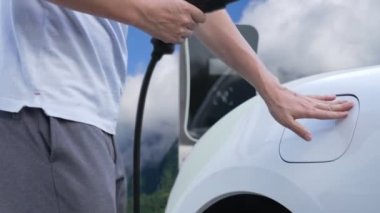 İlerici adam şarj noktasında elektrikli araba yüklüyor, daha temiz bir çevre için temiz ve yenilenebilir enerjiyle çalışan bir EV ile doğada ve dağlarda seyahat ediyor..