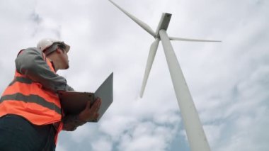 Gökyüzü arka planına sahip bir rüzgar türbini üzerinde çalışan mühendis. Yenilenebilir ve sürdürülebilir enerjinin gelecekteki üretimi için yenilikçi bir ideal. Rüzgar türbininden enerji üretimi.