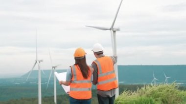 Erkek ve kadın mühendisler kırsal kesimdeki bir tepenin tepesinde ya da dağda rüzgar çiftliğinde çalışıyorlar. Yenilenebilir ve sürdürülebilir enerjinin gelecekteki üretimi için yenilikçi idealler.