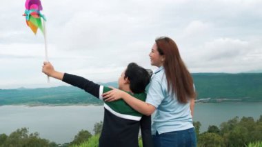 İlerici bir kadın ve oğlu tatilde, çocuk oyuncak bir yel değirmeni taşırken tepenin dibinde gölün doğal güzelliğinin tadını çıkarıyorlar..
