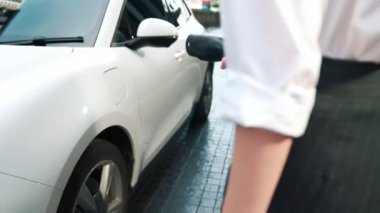 İlerici iş kadını şehir merkezinde dolaşmadan önce şarj cihazından elektrikli arabasına şarj prizi takıyor. Çevre dostu şarj edilebilir araba, sürdürülebilir ve temiz enerjiyle çalışıyor..
