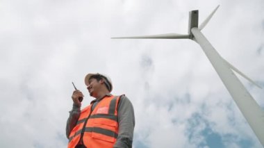 Gökyüzü arka planına sahip bir rüzgar türbini üzerinde çalışan mühendis. Yenilenebilir ve sürdürülebilir enerjinin gelecekteki üretimi için yenilikçi bir ideal. Rüzgar türbininden enerji üretimi.
