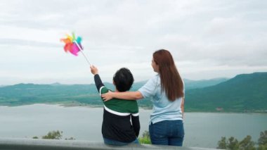 İlerici bir kadın ve oğlu tatilde, çocuk oyuncak bir yel değirmeni taşırken tepenin dibinde gölün doğal güzelliğinin tadını çıkarıyorlar..