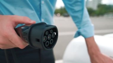 İlerici işadamı, şehir merkezinde dolaşmadan önce şarj cihazından elektrikli arabasına şarj prizi takıyor. Çevre dostu şarj edilebilir araba, sürdürülebilir ve temiz enerjiyle çalışıyor..