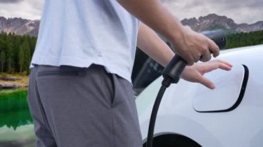 İlerici adam şarj noktasında elektrikli araba yüklüyor, daha temiz bir çevre için temiz ve yenilenebilir enerjiyle çalışan bir EV ile doğada ve dağlarda seyahat ediyor..