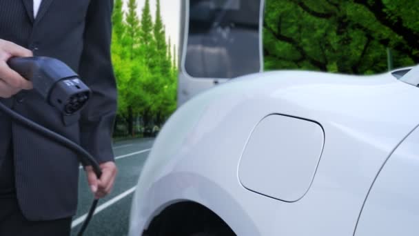 進歩的なビジネスマンは 緑の森の近くの充電ポイントから彼の電気自動車を充電するのを停止します 将来の環境を守るために持続可能でクリーンなエネルギーによって駆動されるEv車 — ストック動画