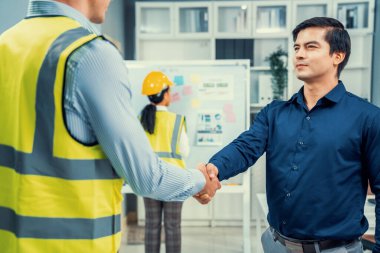 An engineer with a protective vest handshake with an investor in his office. Following a successful meeting, employee and employer form a partnership.