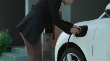 Bir kadın evinde elektrikli araç şarj aletinin fişini çekiyor. İlerici bir yaşam tarzında elektrikli araçların kullanımı, temiz ve sağlıklı bir çevreye katkıda bulunur..