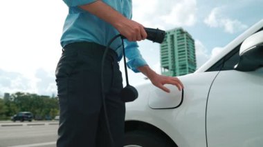 İlerici işadamı, şehir merkezinde dolaşmadan önce şarj cihazından elektrikli arabasına şarj prizi takıyor. Çevre dostu şarj edilebilir araba, sürdürülebilir ve temiz enerjiyle çalışıyor..