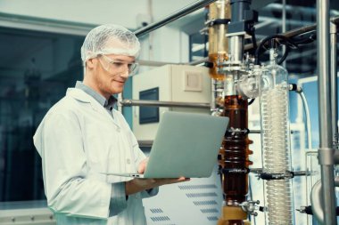 CBD yağ çıkarıcısının yanında dizüstü bilgisayarla çalışan eczacı bilim adamı ve tıbbi esrar ürünleri üretmek için kullanılan bilimsel bir makine.