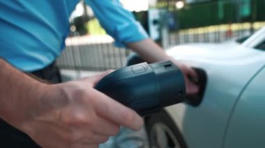 İlerici işadamı, şehir merkezinde dolaşmadan önce şarj cihazından elektrikli arabasına şarj prizi takıyor. Çevre dostu şarj edilebilir araba, sürdürülebilir ve temiz enerjiyle çalışıyor..