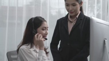 Hevesli Asyalı bayan yönetici yeni çalışana ofiste nasıl verimli müşteri hizmetleri operatörü olunacağını öğretiyor. Genç bayan çağrı merkezi kulaklık kullanarak müşteri desteği sağlıyor..