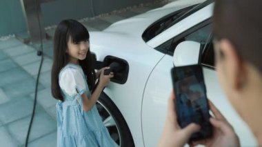 Evde şarj edilen elektrikli bir araçla okuldan yeni dönen anne ve kızın ilerici yaşam tarzı. Elektrikli araç, sürdürülebilir temiz enerjiyle çalışıyor..