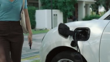 Evinde şarj edilen elektrikli bir araçla işten yeni dönen modern bir kadının ilerici yaşam tarzı. Elektrikli araç, sürdürülebilir temiz enerjiyle çalışıyor..