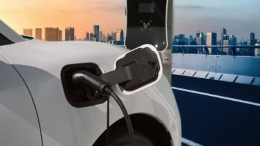 Elektrikli araç, EV araba şehir merkezindeki şarj istasyonunda şarj oluyor. Etrafı yüksek gökdelenlerle çevrili. Çevre dostu yenilikçi temiz enerji kavramı.