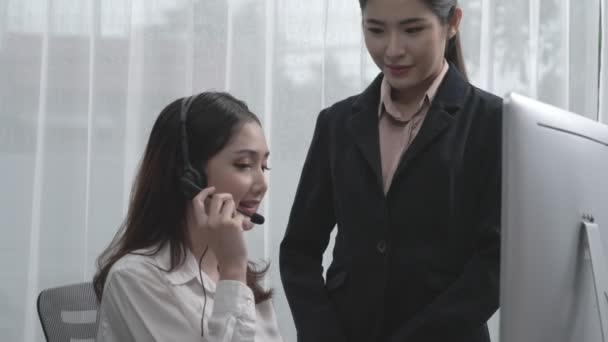 オフィスで生産的な顧客サービスオペレーターになる方法を新しい従業員に教える熱狂的なアジアの女性マネージャー ヘッドセットを使用してカスタマーサポートを提供する若い女性コールセンター — ストック動画
