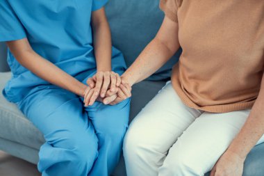 A contented senior woman visited by her personal caregiver and hold each others hands.