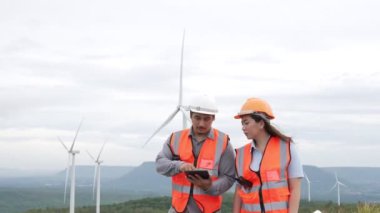 Erkek ve kadın mühendisler kırsal kesimdeki bir tepenin tepesinde ya da dağda rüzgar çiftliğinde çalışıyorlar. Yenilenebilir ve sürdürülebilir enerjinin gelecekteki üretimi için yenilikçi idealler.