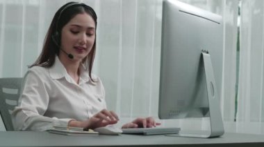 Masasında dizüstü bilgisayarla çalışan kulaklık ve mikrofon takan Asyalı müşteri destek operatörü. Hevesli kadın çalışanlar müşteri hizmetleri sunuyor, destekleyici çağrı merkezi temsilcisi müşterilere yardım ediyor.