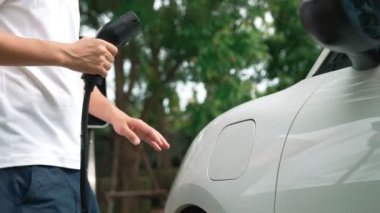 İlerici adam elektrikli aracına elektrik kablosu takıyor. Ev şarj istasyonundan EV arabası. Çevreyi korumak için temiz ve yenilenebilir enerji kullanan elektrikli bir araba. Çevre dostu otomobil.