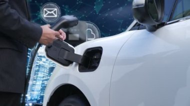 İlerici işadamı, arka planda ağ sembolleri olan şehir ve İnternet 'ten gelen yenilenebilir enerji kaynaklı şarj cihazını elektrikli aracına yüklüyor. Modern çevre dostu kavram.
