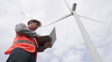Gökyüzü arka planına sahip bir rüzgar türbini üzerinde çalışan mühendis. Yenilenebilir ve sürdürülebilir enerjinin gelecekteki üretimi için yenilikçi bir ideal. Rüzgar türbininden enerji üretimi.