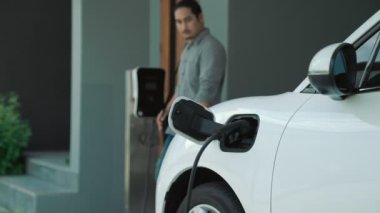 Adamın biri evinde elektrikli araç şarj aletinin fişini çekiyor. İlerici bir yaşam tarzında elektrikli araçların kullanımı, temiz ve sağlıklı bir çevreye katkıda bulunur..