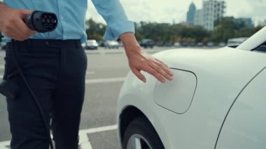 İlerici işadamı, şehir merkezinde dolaşmadan önce şarj cihazından elektrikli arabasına şarj prizi takıyor. Çevre dostu şarj edilebilir araba, sürdürülebilir ve temiz enerjiyle çalışıyor..