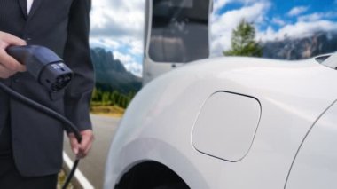 İş dünyasındaki yenilikçi adam elektrikli arabasını dağlarla dolu bir kırsal kesimdeki şarj istasyonundan alıyor. Yol yolculuğu, EV arabalı macera yenilenebilir enerjiyle çalışıyor..