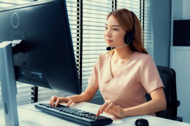 Competent female operator working on computer and while talking with clients. Concept relevant to both call centers and customer service offices.